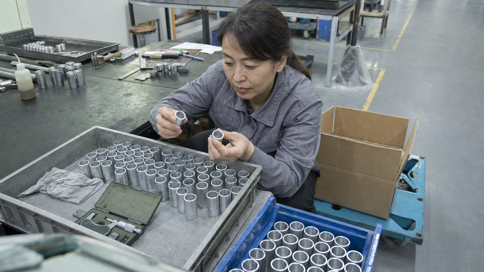 女质量检验员在车间包装台旁核对6061铝合金精密套筒和分区料盘