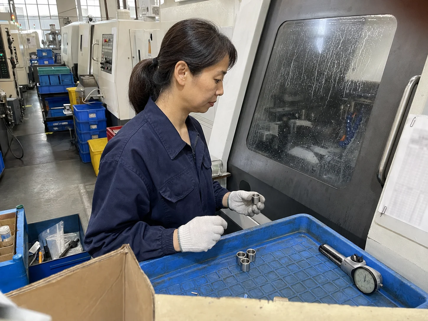 女工艺技术员在关闭舱门的走心机旁核对精密不锈钢衬套和首件料盘